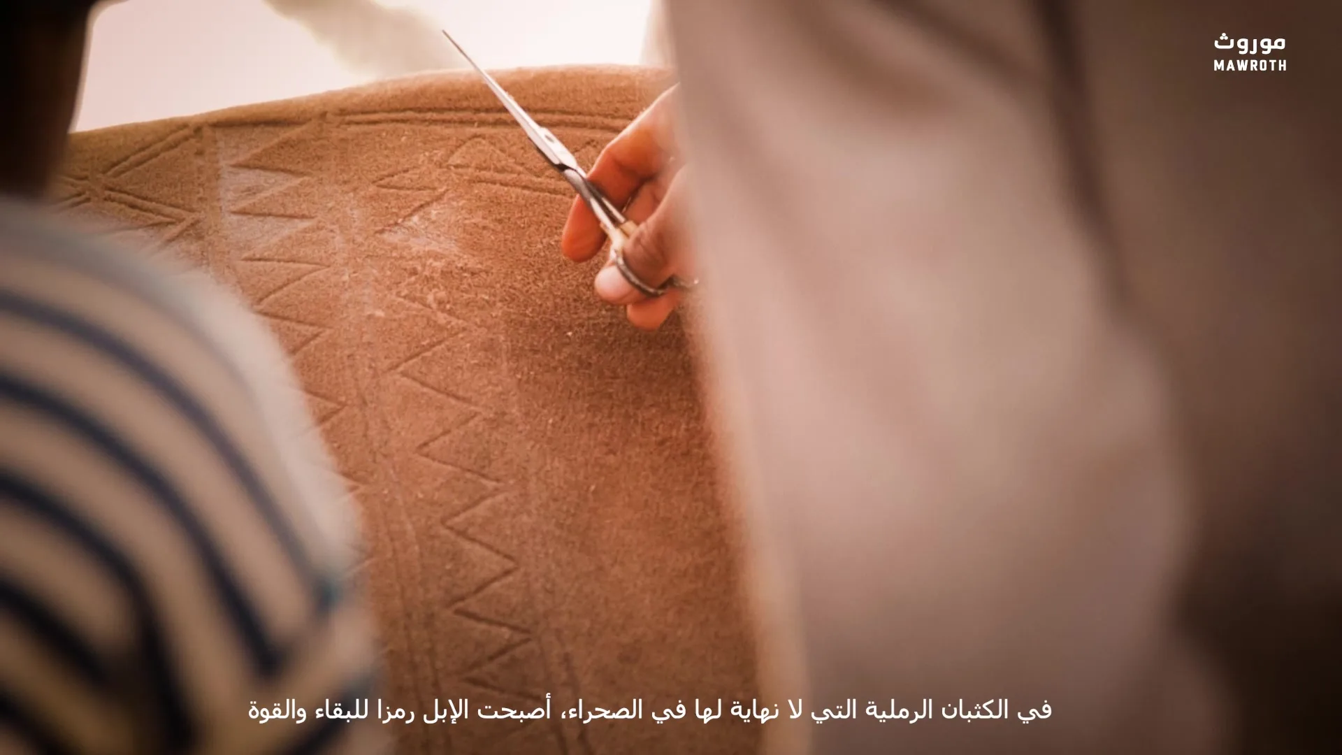Close-up of scissors cutting geometric zigzag motifs into camel hide, hands of the artisan visible