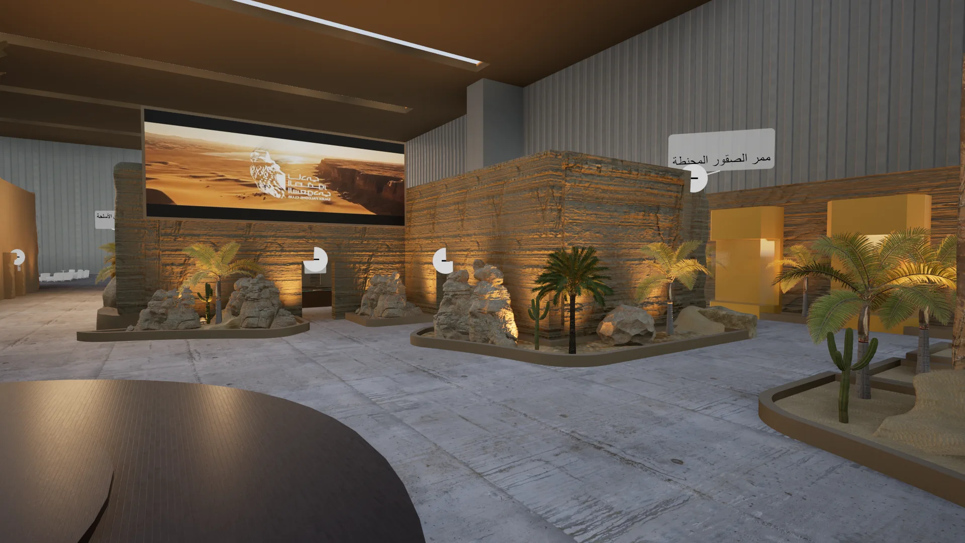Interior hall view showing a large desert landscape projection screen, directional Arabic signage and desert-rock landscaping with palm trees and cacti