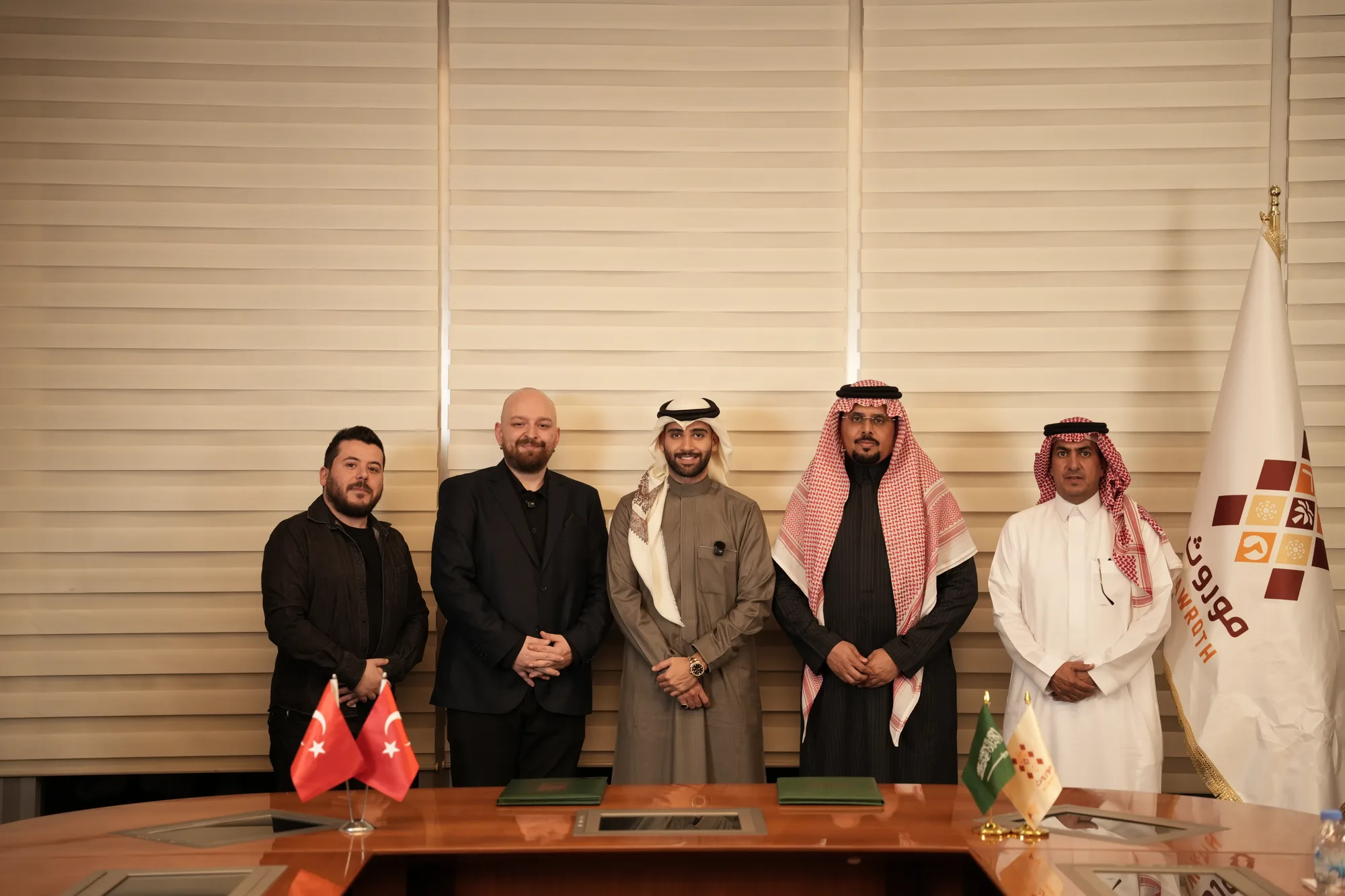 Five-person formal group portrait standing behind the signing table, Mawroth flag and mark visible