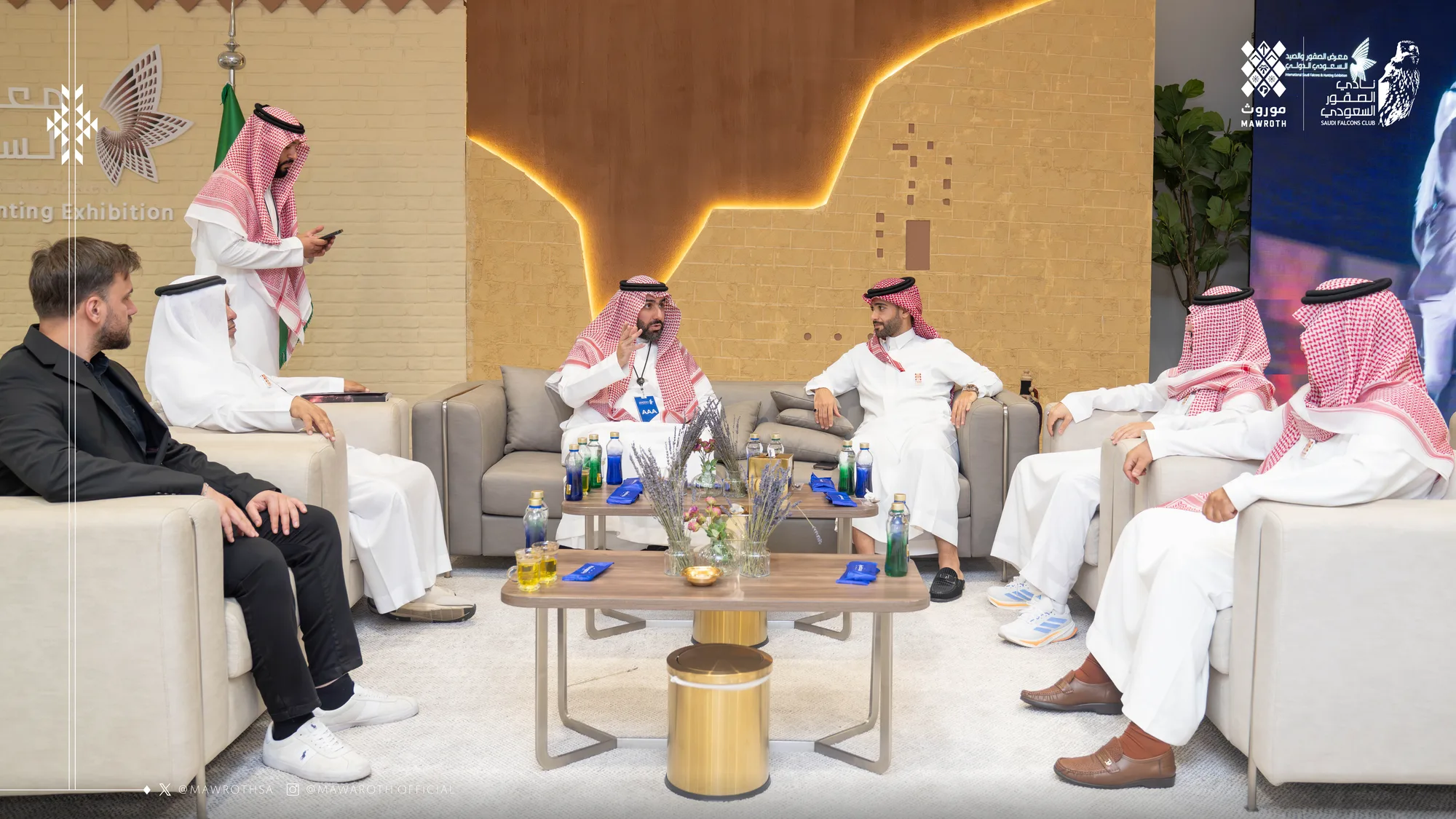 Wide view of the partnership meeting in progress — both delegations seated in the exhibition lounge with a standing official addressing the group